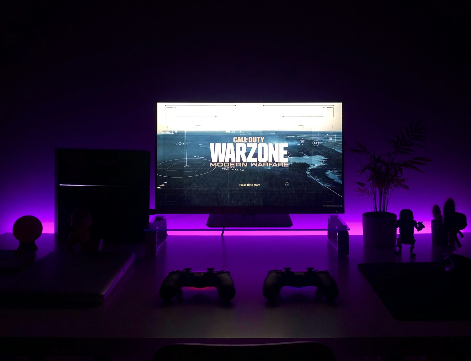 MacBook, gaming controller, earbuds and smartphone on a dark surface